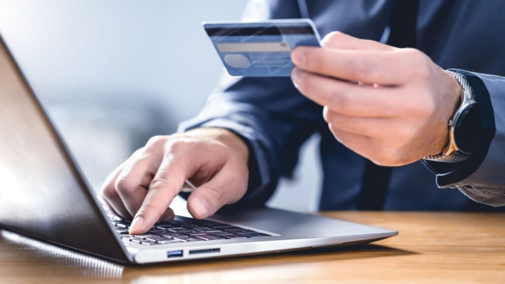 a man holding a credit card in front of his laptop
