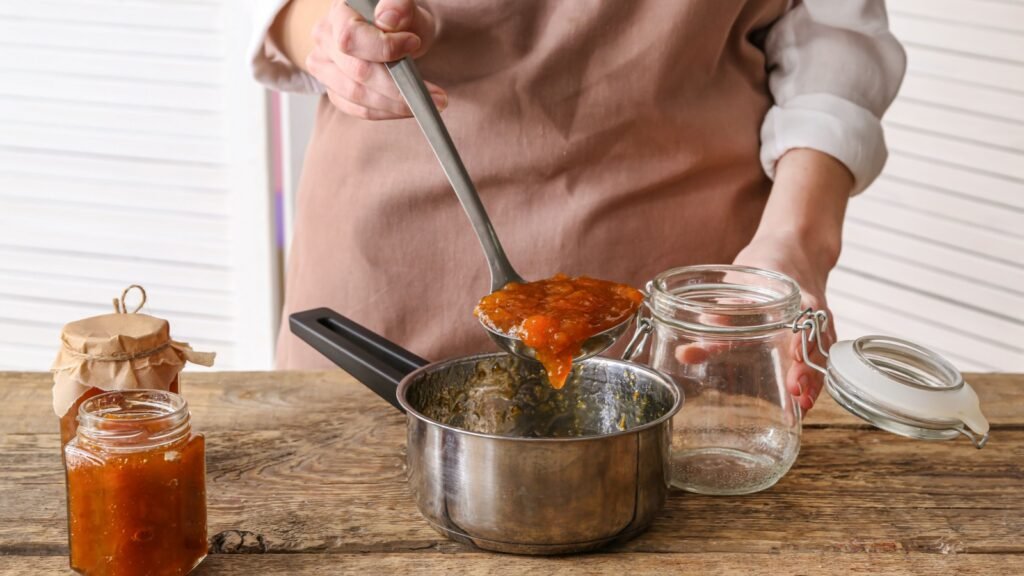 woman pouring peach jam into jar
